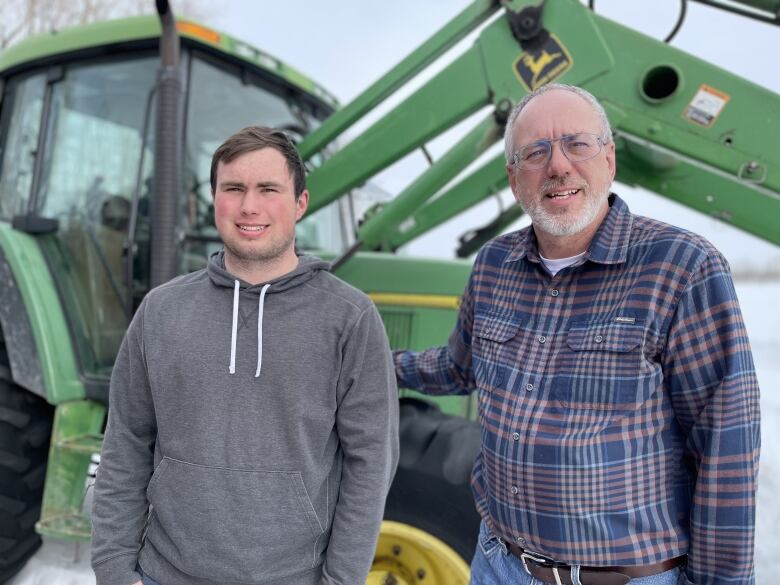 Maxwell Olson (left) and father Mark Olson pose on their family farm in front of a green tractor.