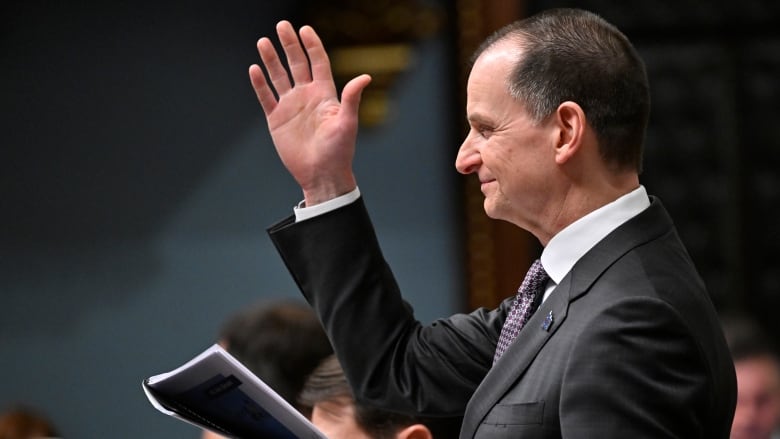 Man in a legislature raises one hand. In profile shot.