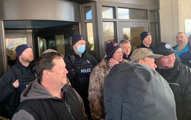 A group of people standing outside of an entrance to a hotel. Police are blocking the door. 