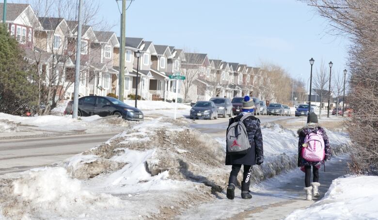 Two kids walk on the sidewalk of a residential street in Steinbach.