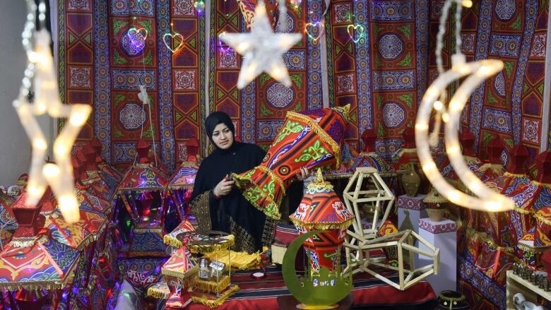 A woman holds a traditional 'famous' lantern surrounded by other lanterns for sale at her workshop.