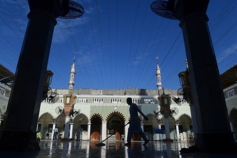 A man sweeps the floor of a mosque in an open courtyard.