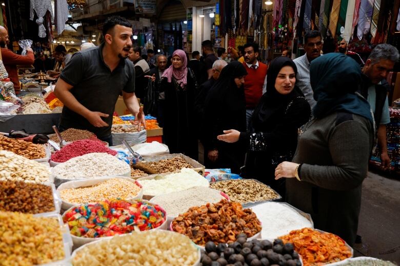 People shopping at a wholesale market with bulk colourful nuts, chips and foods on display at a stall.