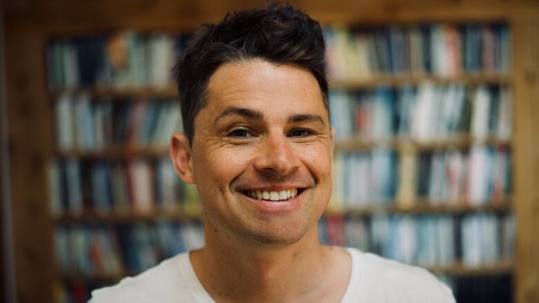 Michael Christie smiles widely into the camera with bookshelves in the background.