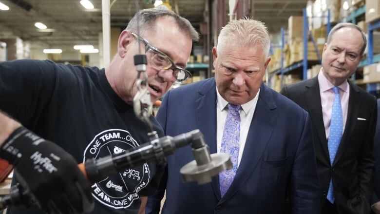 Ontario premier Doug ford watches an employee demonstrate an island drain assembly