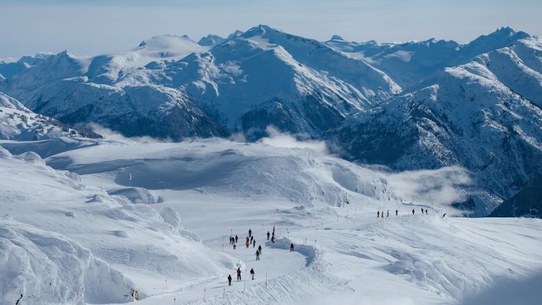 People on skis or snowboards are pictured navigating a path across a mountain on a sunny day.