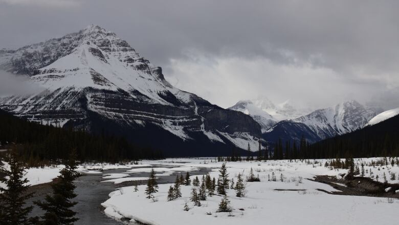 A frozen river winds in front of snow covered mountains. 