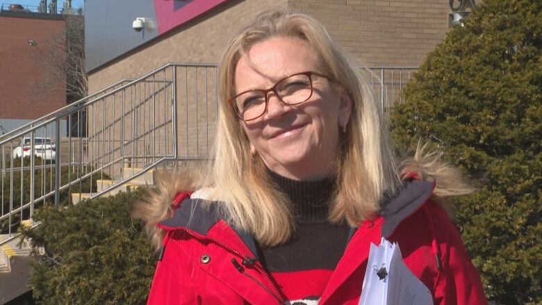 A woman with glasses stands outside looking just off camera