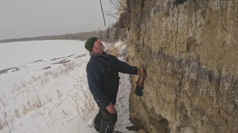 A man with a green cap holds a bone and inspects a hill slant.