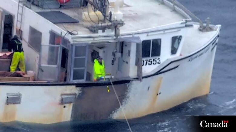 A fishing vessel is seen floating in the water. Two people are seen on deck. 