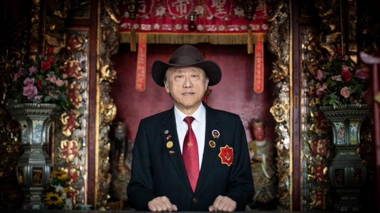 A man with a hat and in a suit stands in front of a red altar.