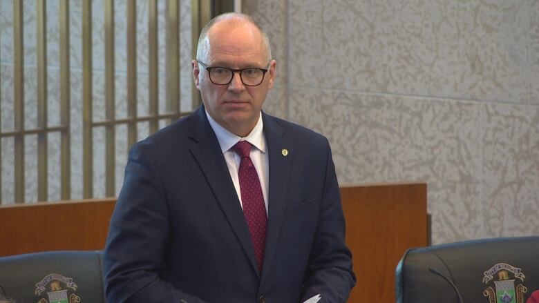 A man in a blue suit is standing and talking.