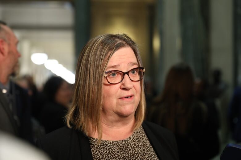 A woman with blonde hair, and dark rim glasses speaks in the rotunda of the Saskatchewan legislature. 