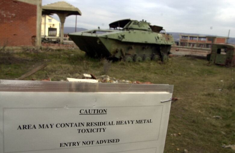 A warning sign in front of a tank, blurred in the background, reads 