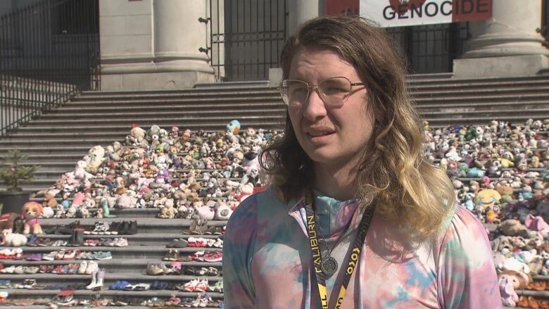 Cherry Bask speaking to camera in front of the steps of the Vancouver Art Gallery where shoes and stuffed animals were laid in tribute to residential school victims at the former Kamloops Indian Residential School. 