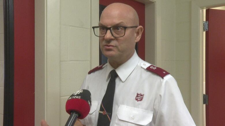 A bald man in a white shirt stands in front of a microphone.