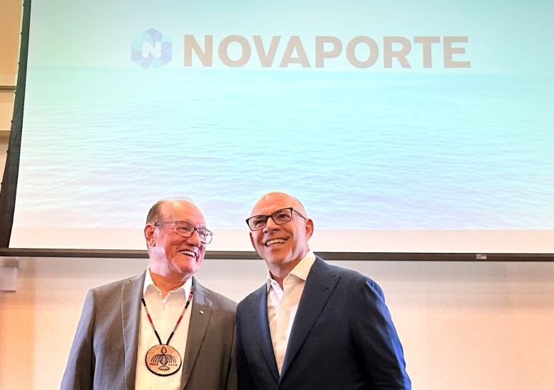 Two men with glasses smile in front of a projector screen with the company name Novaporte on it.