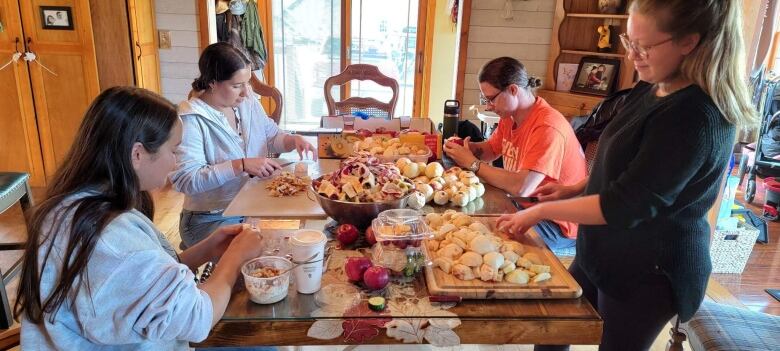 Four adults gathered around a dining table peel apples.