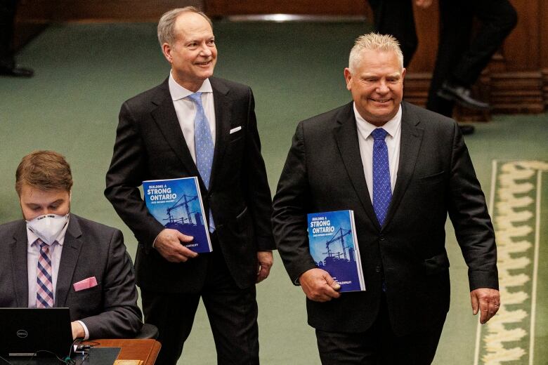 Two men hold budget books.