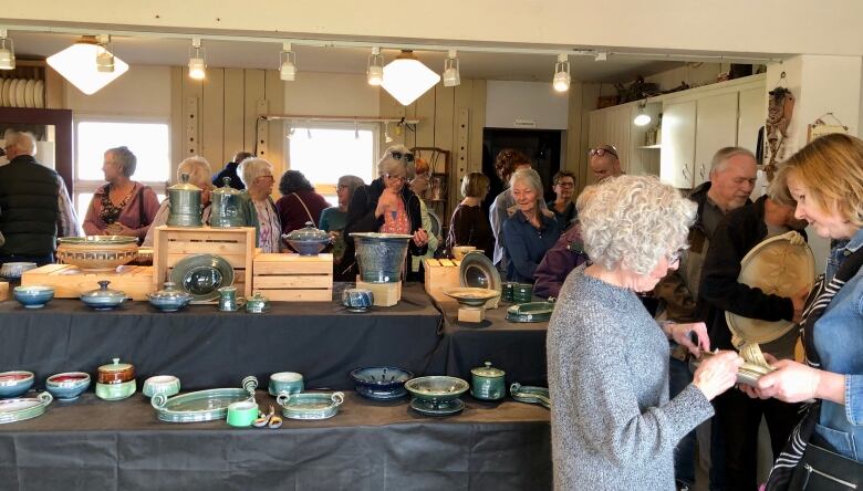 A group of people peruse shelves of ceramic bowls and plates.