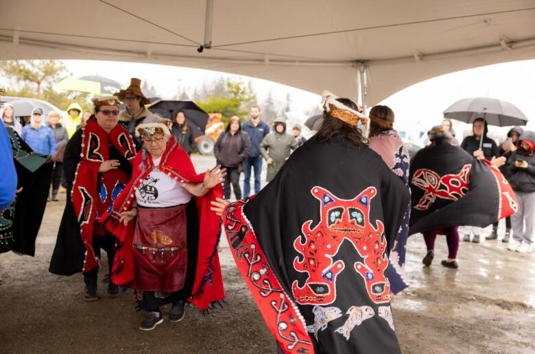 Women in indigenous cloaks dance with their hands up in a circle under a small white tent