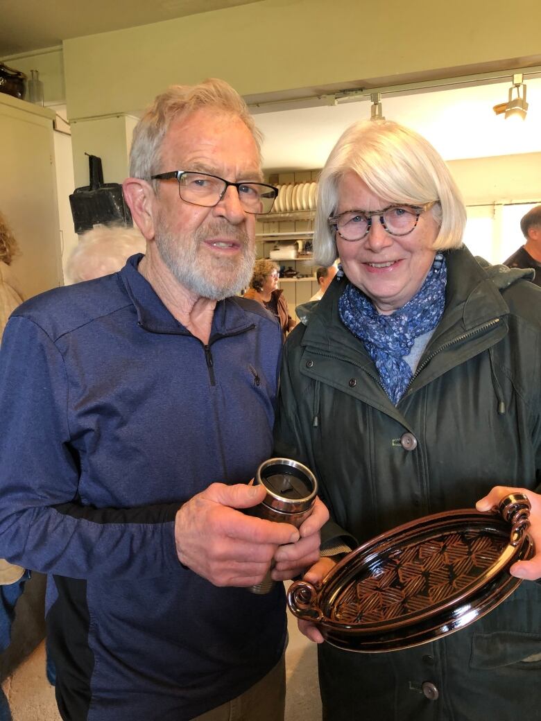 Herman Venema and a woman stand side by side holding a ceramic cup and bowl and smiling at the camera