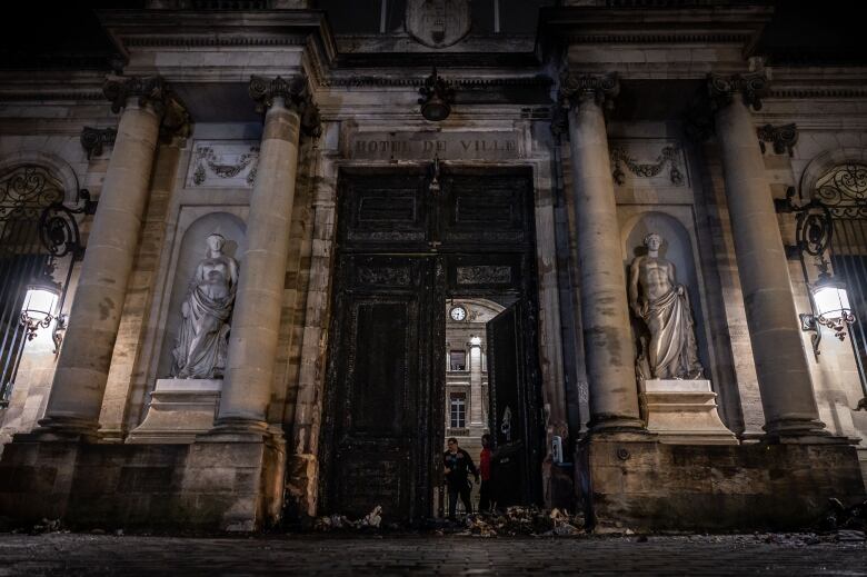 A historic building with large columns is shown charred and blackened in a nighttime photo.