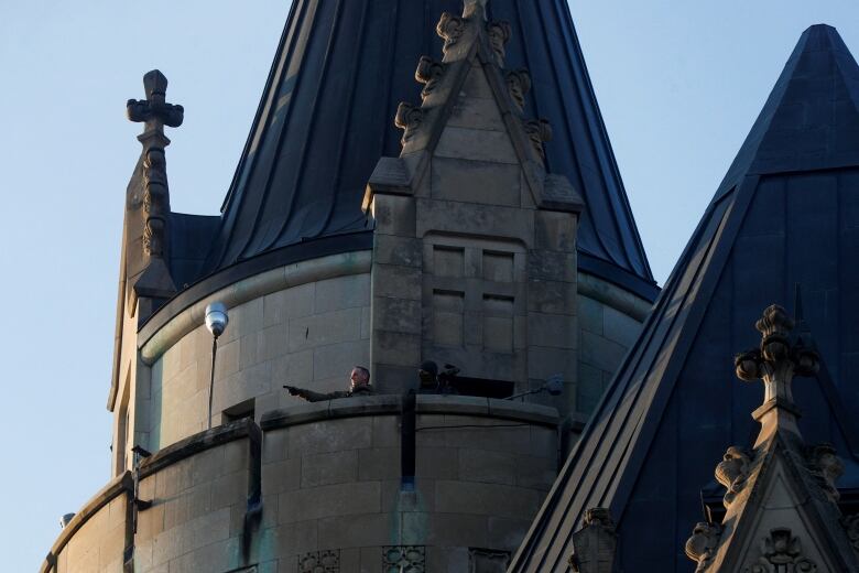 A police or security officer points from a roof.