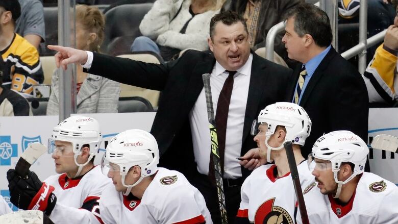 One hockey coach points to his right as another coach listens.