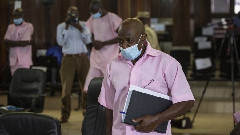 A man carrying a notebook and wearing a COVID mask is shown in a courtroom.