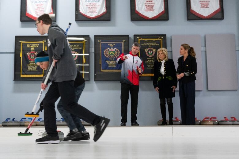 Two women listen to someone talk about curling next to a rink.