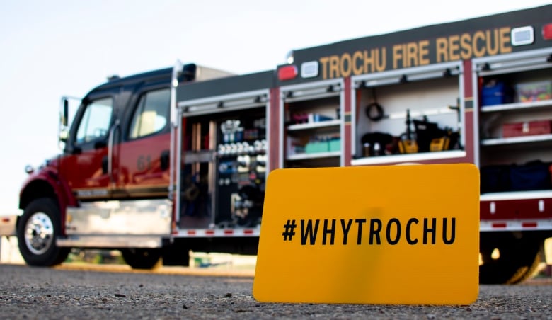 A sign saying Why Trochu sits in front of a fire truck.