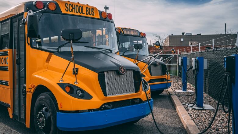 A yellow electric school bus charges at a charging station.