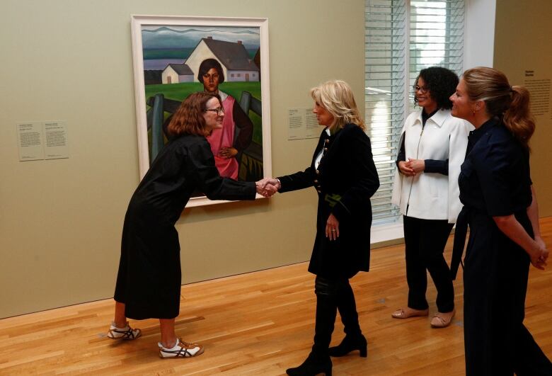 A dignitary shakes a gallery curator's hand in front of a painting.