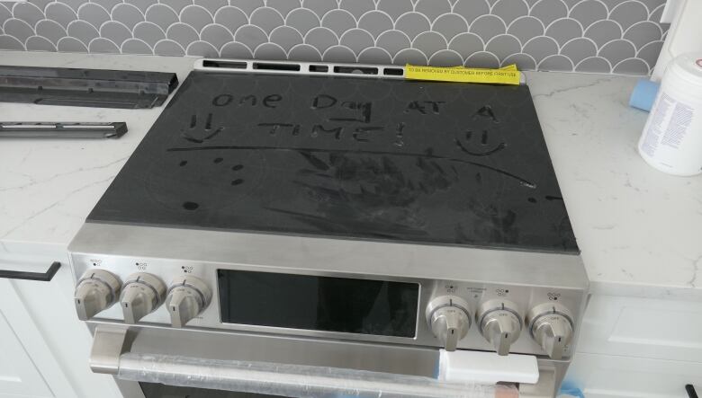 A stovetop is covered in dust with a handwritten message in the dust saying 'take one day at a time'.