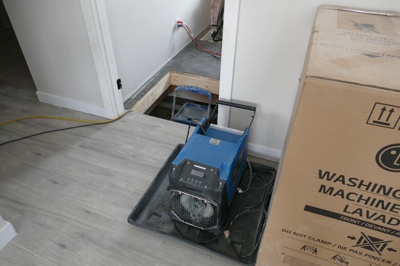 An electric dehumidifier is plugged in and sitting on the floor of the house.