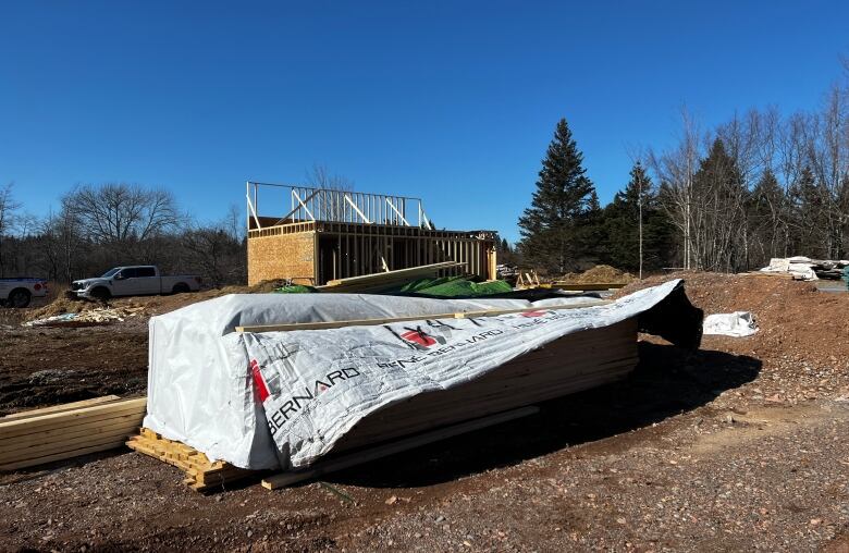 A tarp lies on top of a pile of lumber in front of a construction site on a sunny day.