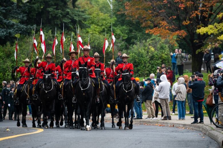 Mounted police officers ride horses along a street while people watch.