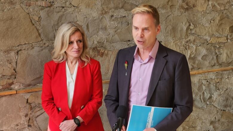 Todd Hirsch, at right, speaks into a microphone while NDP leader Rachel Notley looks on. 