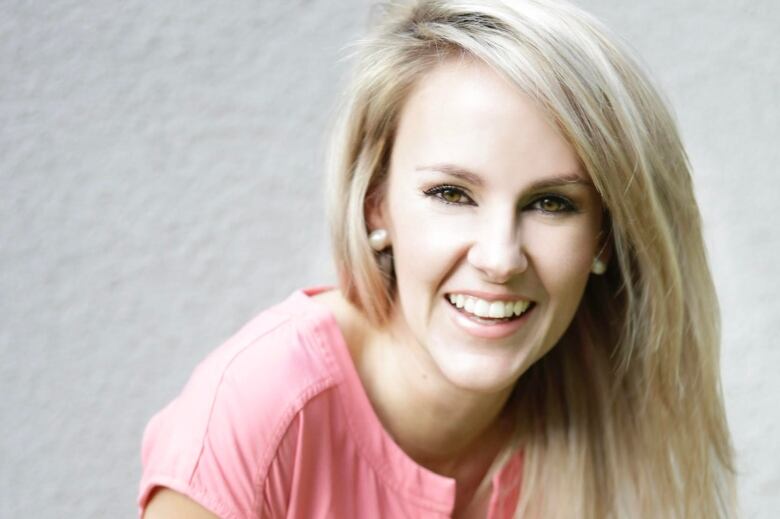 a woman smiles in this headshot. she is wearing a pink shirt and has blonde hair 