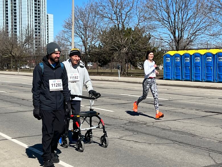 Older man with a walker smiles while running alongside a young man.