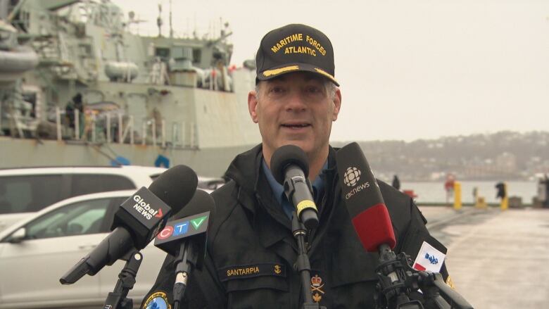 A man in uniform speaks to a number of microphones.