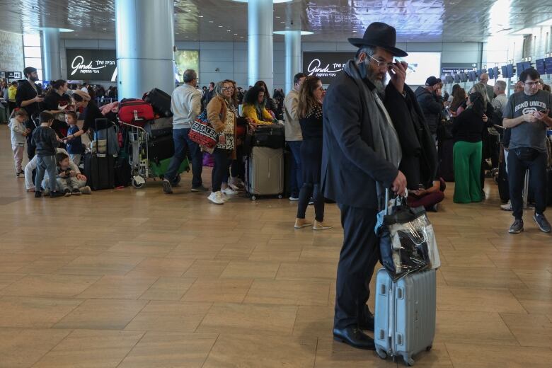 A man in a hat with luggage is shown in the foreground at an airport, with lines of people shown behind him.