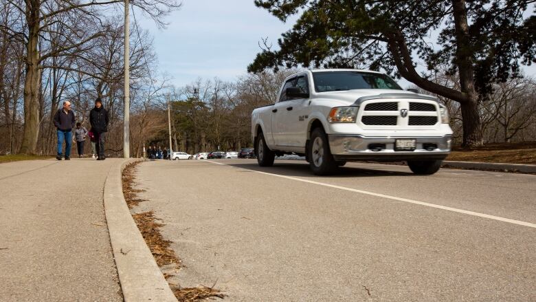 A car drives past pedestrians in High Park. 