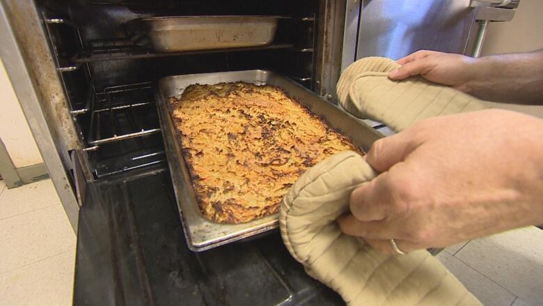 A pan resembling shepherd's pie is pulled out of an oven.