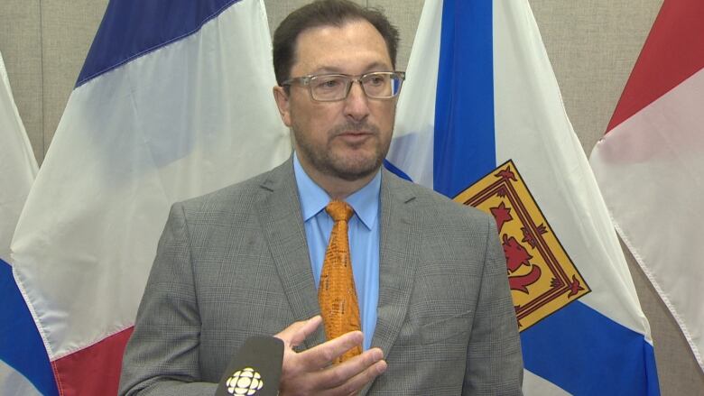 A man with glasses and a beard stands in front of flags.