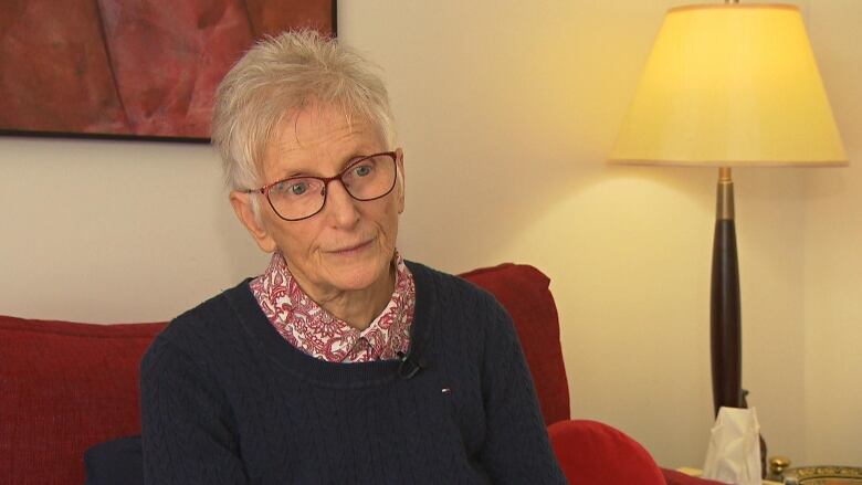 A woman sits on a couch and looks at the camera. 