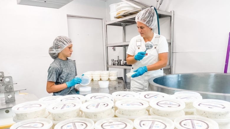 A woman and a child stand in a white room with dozens and dozens of cream cheese containers