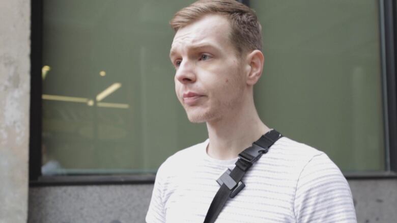 A red-haired man in a white T-Shirt poses outside a building.