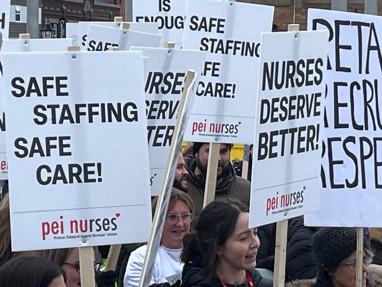 A crowd of nurses hold up protest signs.